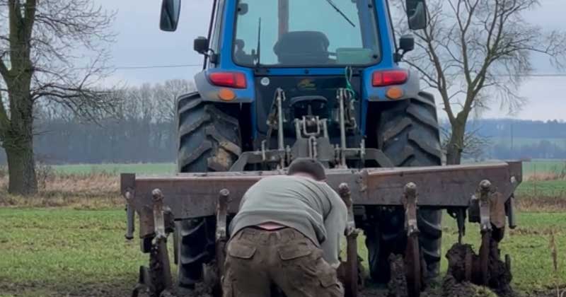 Il trattorista ara la terra vicino al fiume, e l’aratro si è impigliato in una catena